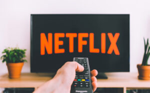Hand with a remote pointing at a TV with Netflix playing.